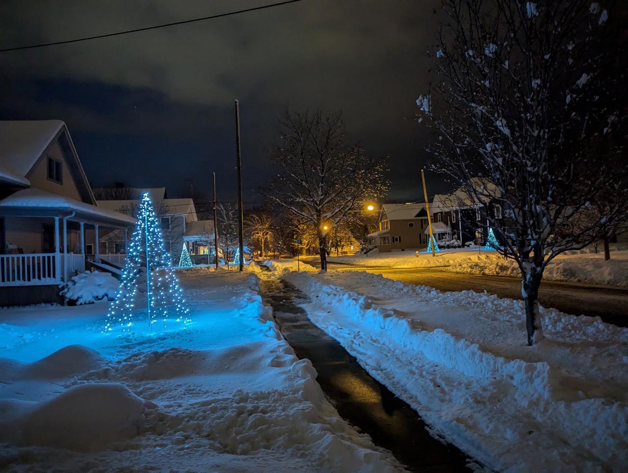 Full cone-shaped Christmas Corner light display at left, with more displays along a snowy street
