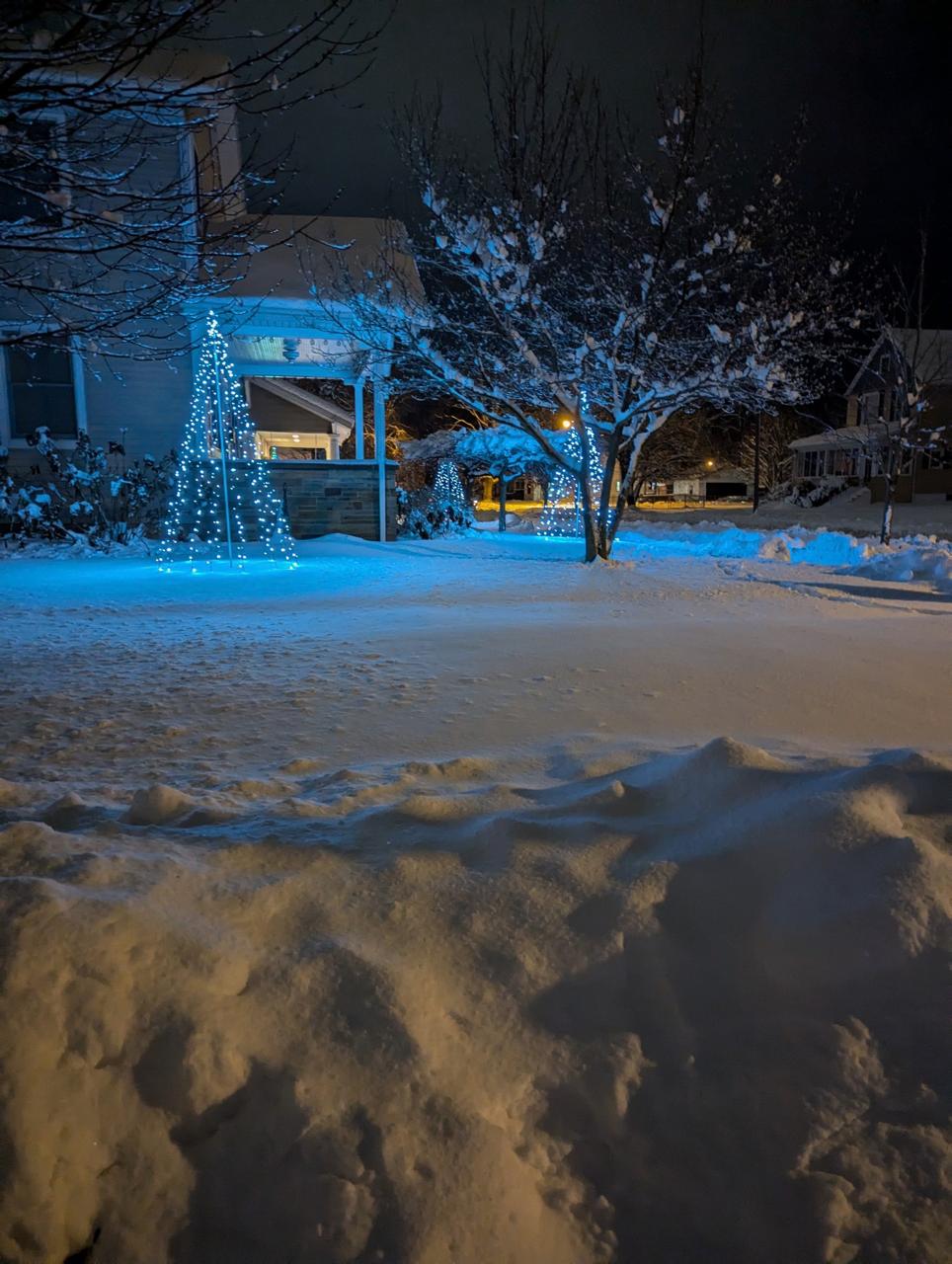 Illuminated cone-shaped Christmas Corner display beside a porch in freshly fallen snow